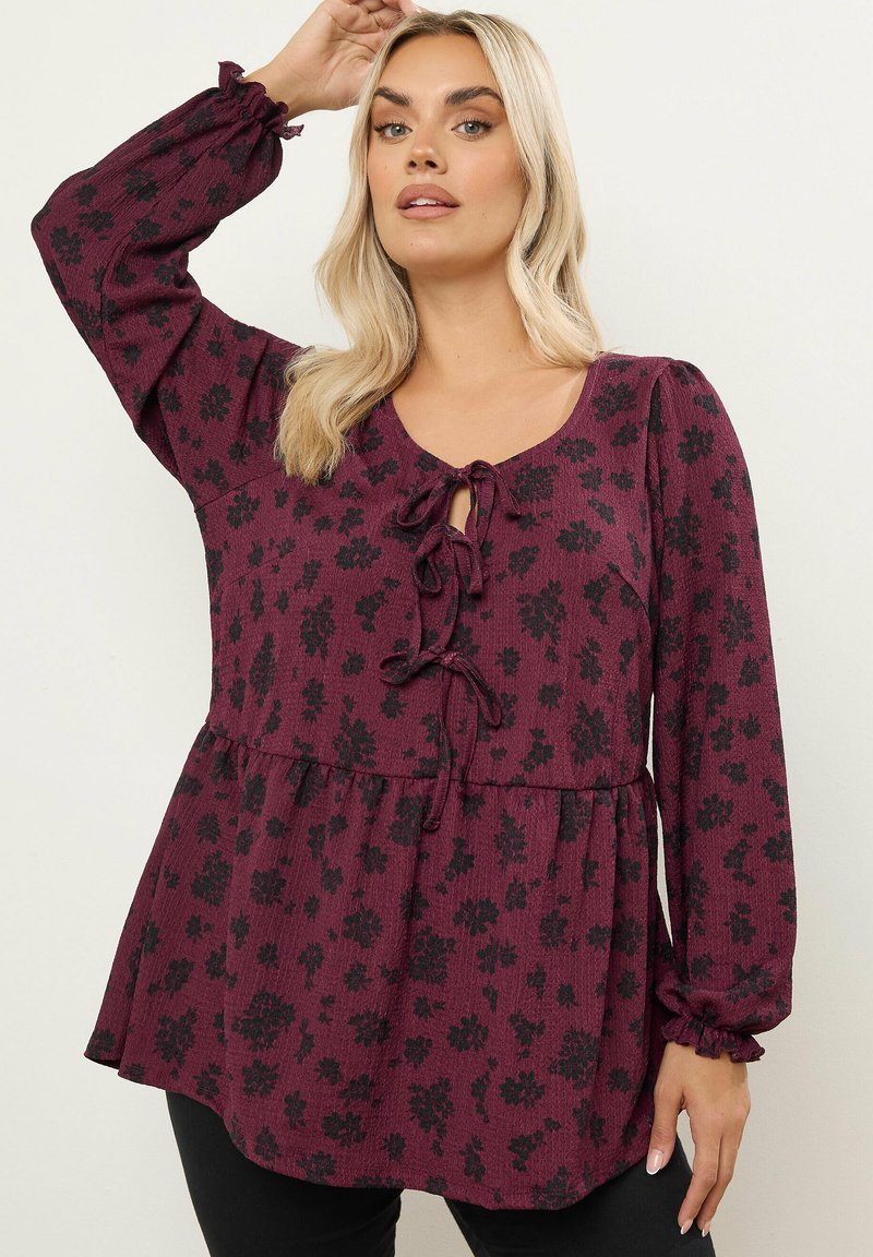 Blusa floreale bordeaux con maniche lunghe, polsini arricciati e nodo frontale. Presenta un tessuto strutturato con vita arricciata per una vestibilità rilassata.