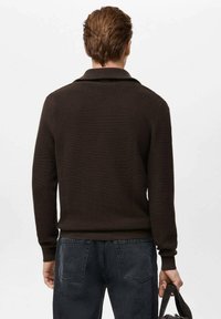 Brązowy sweter o teksturowanej fakturze z prążkowanym kołnierzem i mankietami, o krótkim kroju. Nosi się go z ciemnymi jeansami i trzyma w czarnej torbie.