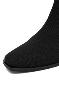 Czarne botki za kostkę z żebrowanym tekstylnym wierzchem, spiczastym noskiem i gładką syntetyczną podeszwą. Posiadają dzianinowy wzór dla dodatkowej elastyczności.