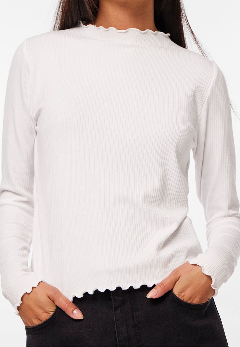 Vit ribbad långärmad topp med en scallop-formad halsringning och nederkant. Materialet har en mjuk textur; åtsittande design med långärmar och sidofickor.