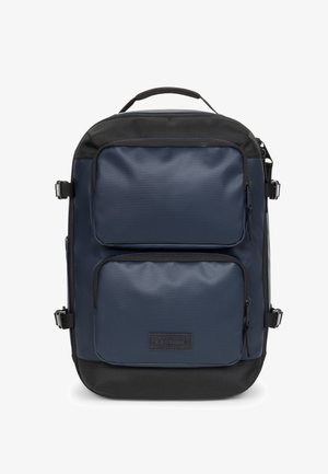 Mochila azul marino con una textura suave, que cuenta con dos bolsillos frontales con cremallera, acentos negros y un asa superior. Fabricada con un material duradero y un diseño minimalista.