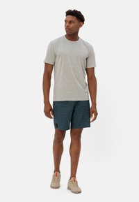 T-shirt grigia in cotone e pantaloni corti texturizzati blu, con un piccolo etichetta nera, abbinati a sneaker beige con dettagli arancioni.