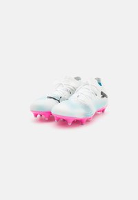Scarpe da calcio bianche con tomaia in mesh testurizzato, accenti in gradiente blu e una suola in gomma rosa brillante con tacchetti conici. Dettaglio del logo nero.