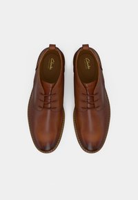 Een paar gepolijste bruine leren veterschoenen met ronde neuzen en gestikte zolen op een witte achtergrond.