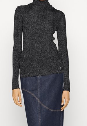 Vrouw met een zwarte, glinsterende coltrui met lange mouwen en een donkerblauwe denim rok met gebogen naaddetails.