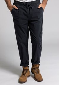 Pantalones azul marino de cintura elástica con bolsillos laterales y puños enrollados, hechos de una tela ligera. Combinados con botas de ante color beige.
