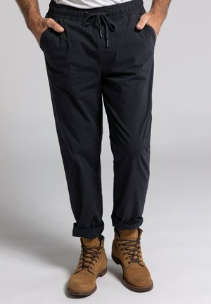 Pantalones azul marino de cintura elástica con bolsillos laterales y puños enrollados, hechos de una tela ligera. Combinados con botas de ante color beige.