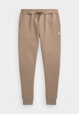 Pantalones deportivos beige ajustados, con cintura con cordón, bolsillos laterales, puños en los tobillos y un pequeño logo blanco bordado en la parte superior del muslo.