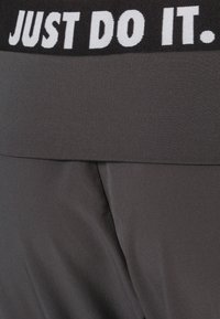Pantaloni sportivi grigi con una vita elastica nera che presenta la scritta "JUST DO IT." in bianco. Tessuto morbido, design aderente, texture leggera.
