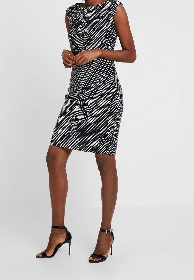 Černobílé přiléhavé šaty s geometrickým liniovým vzorem, s krátkými rukávy a délkou ke kolenům. V kombinaci s černými lodičkami na kotníkovém pásku.