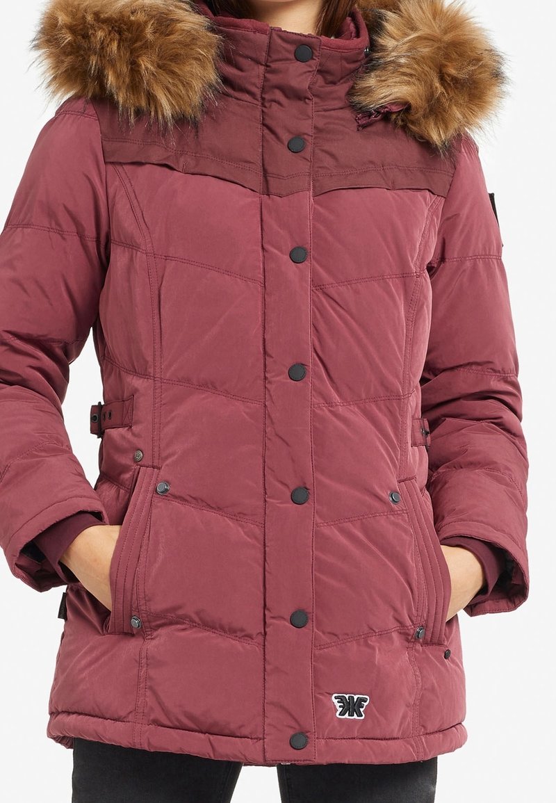 Chaqueta tipo puffer color granate con capucha de piel sintética, cierre de cremallera y botones, bolsillos laterales y diseño acolchado para mayor calidez.