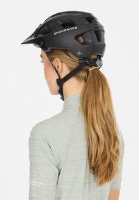 Schwarzer Fahrradhelm mit Belüftungsschlitzen und einem Visier. Verfügt über verstellbare Riemen und einen sicheren Sitz. Wird von einer Person mit langen Haaren getragen.
