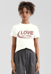 Weißes Baumwoll-T-Shirt mit einem abgenutzten roten Grafikdesign, das den Text "LOVE" und "est 1994" zeigt, Rundhalsausschnitt und kurze Ärmel.