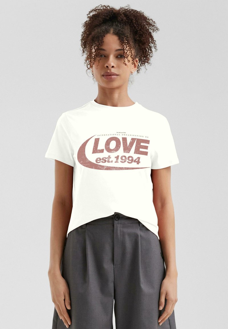 Weißes Baumwoll-T-Shirt mit einem abgenutzten roten Grafikdesign, das den Text "LOVE" und "est 1994" zeigt, Rundhalsausschnitt und kurze Ärmel.