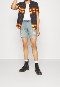 Person wearing a black and orange tie-dye short-sleeve shirt over a white top, distressed denim shorts, white socks, and black lace-up boots.