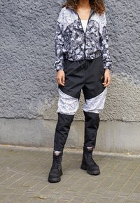 Svart och vit blommönstrad zip-up-jacka med elastiska ärmslut, som matchas med svarta byxor med vita accentpaneler och knälappar. Svarta stövlar.