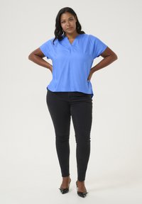 Blå kortärmad blus med notch-krage, slät textur, avslappnad passform, matchad med svarta skinny jeans och svarta klackskor.