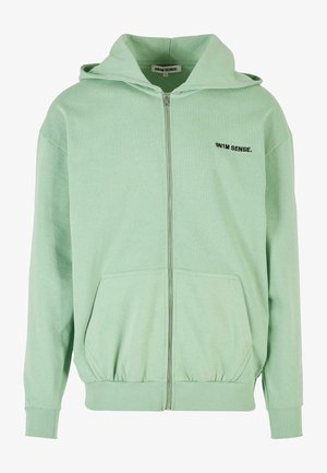 Vaaleanvihreä vetoketjullinen huppari, joka on valmistettu pehmeästä kankaasta, ominaisuuksina rento leikkaus, kengurupocketit ja musta brodeerattu logo rinnassa.