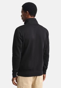 Sudadera negra con cuello alto, hecha de tela suave. Presenta puños y dobladillo acanalados, textura lisa y un diseño minimalista.