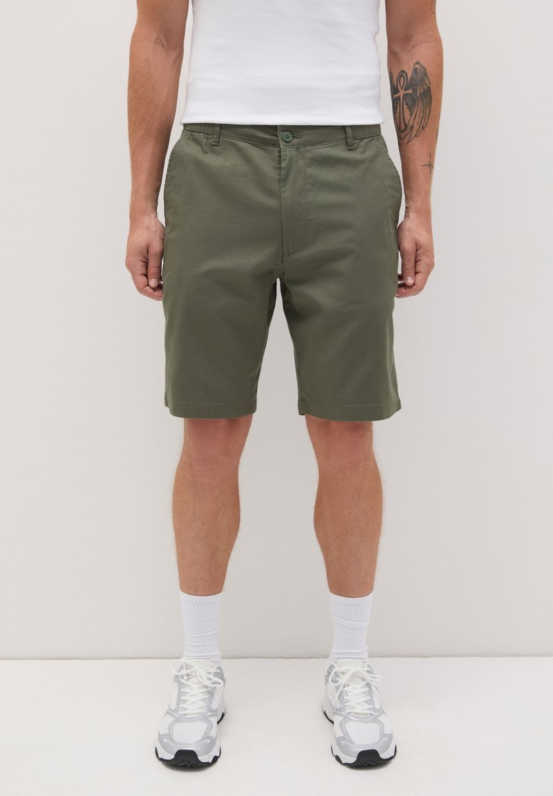 Shorts olive en coupe décontractée, fabriqués en coton avec une texture lisse. Équipés d'une fermeture à bouton et de poches latérales.