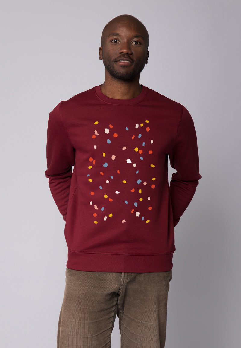 Sweatshirt bordeaux avec un motif abstrait texturé et coloré de formes en rose, bleu, jaune et rouge. Manches longues, encolure ras du cou.