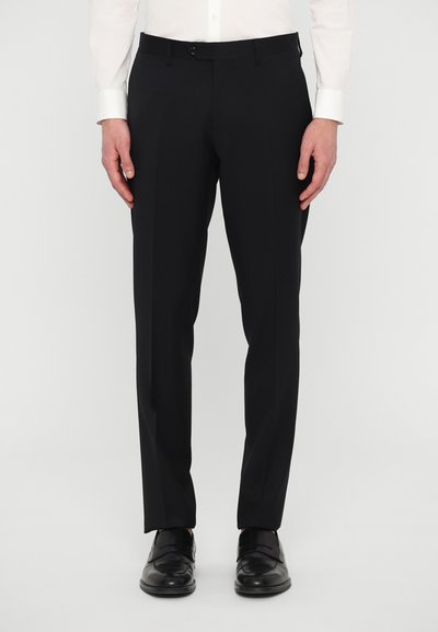 Pantalones negros ajustados con un corte slim, presentan un frente plano, lazos para el cinturón y cremallera. Combinados con zapatos negros pulidos.