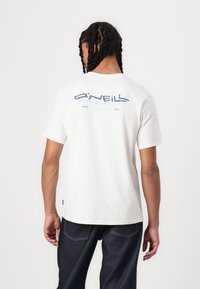 Hvid bomulds t-shirt med et blåt grafisk logo på ryggen, korte ærmer og en afslappet pasform. Sammen med mørkeblå denim jeans.