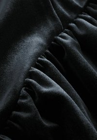 Schwarzer Stoff mit glatten und strukturierten Abschnitten, der entlang einer Kante mit Rüschendetails versehen ist und so ein gestuftes Aussehen erzeugt.