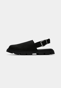 Czarne buty slingback o gładkiej fakturze, szerokiej cholewce, solidnej podeszwie oraz metalowym zapięciu na pięcie. Lekki i nowoczesny design.