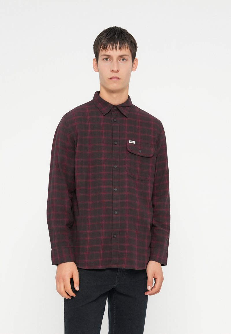 Camicia a quadri rossa e nera con colletto a bottoni, maniche lunghe, taschino singolo sul petto e etichetta del marchio sulla tasca. Tessuto strutturato.