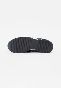 Suela de zapatilla azul marino con superficie de goma texturizada y estrías horizontales para mayor agarre, con un logo grabado en el lateral.