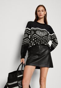 Maglione a pattern bianco e nero con una texture pelosa, abbinato a una gonna di pelle nera aderente e con una borsa a strisce.