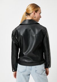 Sort læderjakke med en figursyet design, synlige sømme og en rygydelse. Den har en notch-krave og trykknapdetaljer.