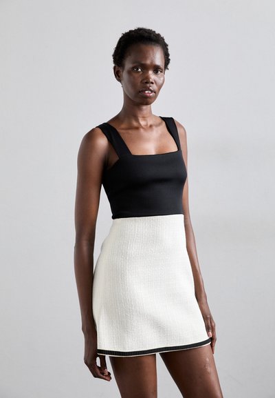 Zweiteiliger Look mit einem schwarzen Rippoberteil mit Quadrat-Ausschnitt und breiten Trägern, kombiniert mit einem weißen strukturierten Rock mit schwarzem Saum.