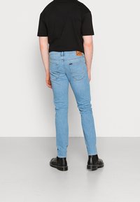 Jeans azzurri chiari con una vestibilità slim, dotati di due tasche posteriori, cuciture in evidenza e un'etichetta in pelle marrone con la scritta "Lee" sulla cintura.