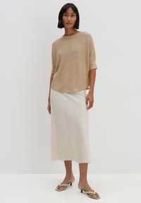 Beige Strickoberteil mit weitem Ausschnitt und halblangen Ärmeln, kombiniert mit einem knielangen elfenbeinfarbenen Rock. Die Schuhe sind beige Sandaletten mit Absatz.