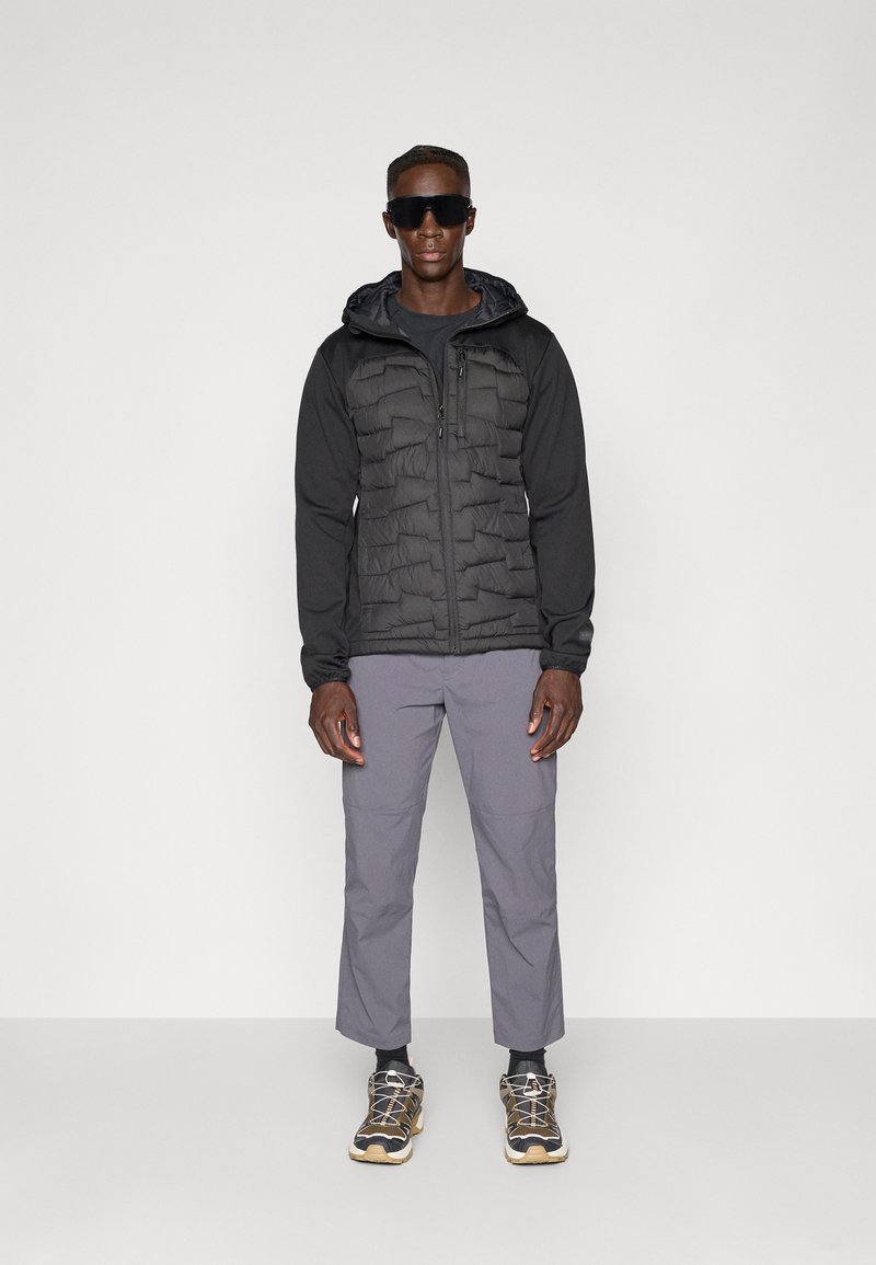 Czarna kurtka puchowa o pikowanej fakturze, długie rękawy, szare spodnie oraz lekkie buty w czarno-szary wzór.