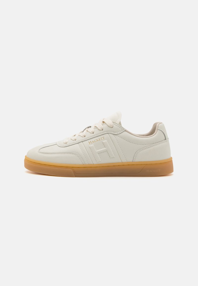 Vit lädersneaker med gummigummisula, rundad tå, snörning framtill och präglad logotyp på sidan. Texturerade detaljer synliga.