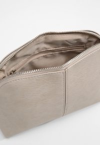 Pochette in pelle beige con una texture liscia, chiusura con zip e una piccola tasca interna. Presenta un design minimalista che enfatizza la funzionalità.