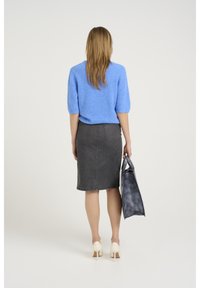 Pull en tricot bleu clair à manches courtes, jupe crayon en denim gris, chaussures à talons haut crème, et sac fourre-tout gris foncé.