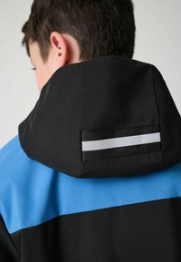 Kapuzenshirt mit einem schwarzen Körper, blauen Schultern und einem gestreiften Akzent auf dem Rücken. Weicher Stoff mit einem klaren, modernen Design.