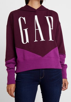 Felpa borgogna e viola con grande scritta bianca "GAP", caratterizzata da un design a blocchi di colore e un cappuccio con coulisse. Texture morbida e vestibilità rilassata.