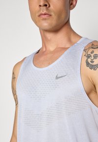 Helles blaues Nike-Top mit einem strukturierten Muster, verfügt über ein graues Logo, ärmelloses Design und einen entspannten Schnitt, das einen glatten Stoff zeigt.