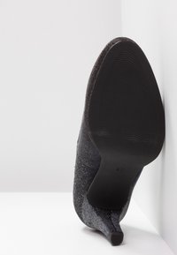 Talons hauts en textile noir avec un bout pointu, présentant une surface texturée et une semelle noire lisse. Taille 37 marquée au bas.