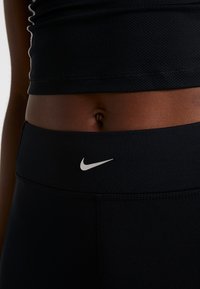 Czarne legginsy sportowe o gładkiej fakturze, z logo na pasie w białym kolorze. Zaprojektowane z myślą o komforcie i swobodzie ruchów.