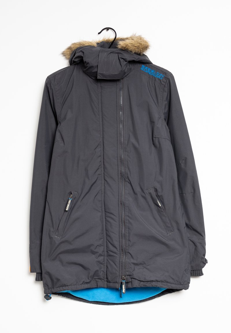 Veste noire avec une capuche en fourrure, dotée de poches zippées et d'une doublure intérieure bleue. Inclus un détail de logo sur le col.