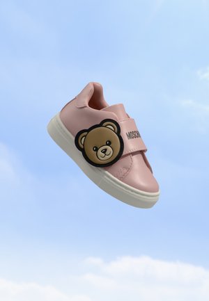 Rosa Kindersneaker mit weißer Sohle, Klettverschluss und Teddybär-Gesicht Dekoration vor klarem blauen Himmel.