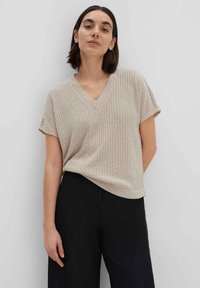 Beige, geribbelde gebreide top met een V-hals en korte mouwen, gecombineerd met zwarte broek. Eenvoudig ontwerp zonder patronen of zichtbare hardware.