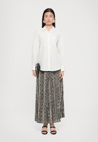 Hvit skjorte med knapp, lange ermer, kombinert med et gulvlangt skjørt med slangertrykk i beige og svart, supplert med svarte sandaler.