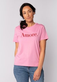 Roze katoenen t-shirt met een ronde hals en korte mouwen. Bevat het woord "Amore." gedrukt in vetrode letters op de borst.